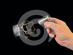 Cylinder and piston in a hand, on a black background. Piston system from a moped. Parts of a motor from a motorcycle, closeup