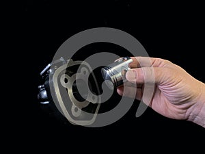 Cylinder and piston in a hand, on a black background. Piston system from a moped. Parts of a motor from a motorcycle, closeup