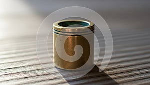 Cylindrical object rests on a textured wooden surface casting a