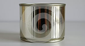 A cylindrical tin can with a metallic, reflective surface is set against a plain white