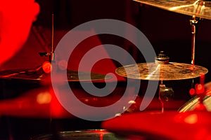Cymbals of a battery lit with the lights of a concert with red details