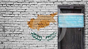 Cyprus flag painted on brick wall and closed door with medical mask protected