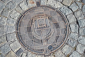 Czech sewer metal hatch with a pattern on the street with paving stones