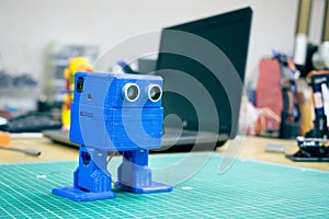 3D printed Funny blue robot on the background of devices and laptop. Robot model printed on automatic three dimensional 3d