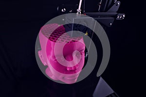 A 3D printer produces a futuristic sculptural humanoid head from pink plastic in foggy light. photo
