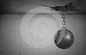 3d rendering of a heavy wrecking ball hangs on its chain from a large uneven ceiling hole.