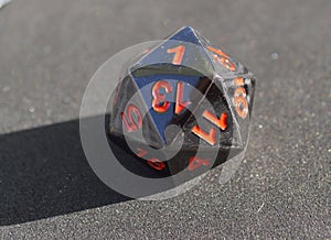D20 twenty-sided black metallic die dice on foam background in bright sunshine - 1 on top face