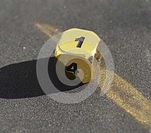 D6 six-sided golden metallic die dice on foam background in bright sunshine - 1 on top face