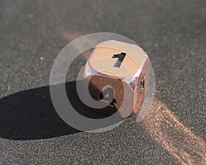 D6 six-sided golden silver copper and black metallic die dice on foam background in bright sunshine - 1 on top face