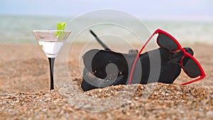 Dachshund wearing sunglasses with cocktail lies on beach