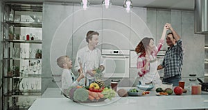 Dacing mature couple in kitchen with their two kids , spending a good morning together while preparing the breakfast.
