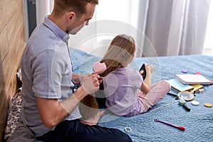 Loving young father brushing and braiding cute little daughter hair enjoy spending time together at home photo