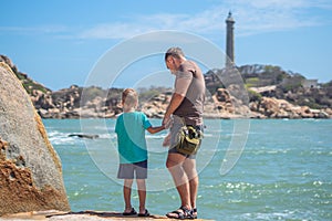 Dad care Son near sea, walk spend time together explore new. Man hold kid hand. Lighthouse background Symbol of
