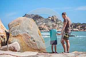 Dad care about Son near sea, walk spend time together explore new. Man hold kid hand, look down. Nature sea rock