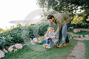 Dad is carrying a little girl pedaling on a bicycle