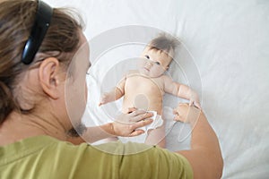 Dad changing diaper on baby girl on bed, changing nappy, everyday care