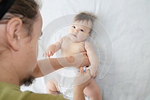 Dad changing diaper on baby girl on bed, changing nappy, everyday life