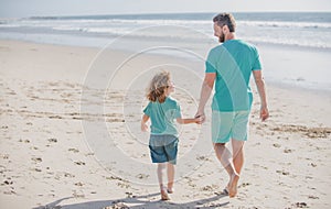 Dad and child boy holding hands and walk together. Father and son walking on summer beach. Concept of friendly family