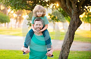 Dad and child having fun outdoors. Father giving son ride on back in park. Portrait of happy father giving son piggyback