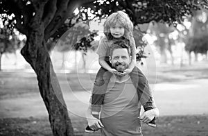 Dad and child having fun outdoors. Father giving son ride on back in park. Portrait of happy father giving son piggyback