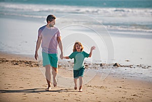 Dad and child holding hands and walk together. Father and son walking on summer beach.