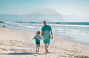 Dad and child holding hands and walk together. Father and son walking on summer beach.