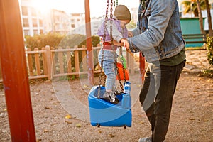 Dad and child are playing on the playground. Swing and slide rides.