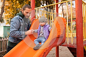 Dad and child are playing on the playground. Swing and slide rides.