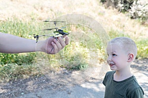 Dad and child playing with radio-controlled helicopter. Blond boy holds in his hand a mini-model of a helicopter in which