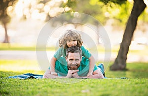 Dad with cute child boy laying on grass in summer park outdoor. Father and son relaxing on nature.