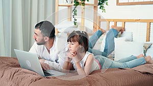 Dad and cute child watch funny video on laptop at home lies on bed, slow motion