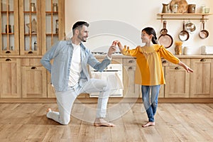 Dad dancing to music with preteen daughter at home kitchen