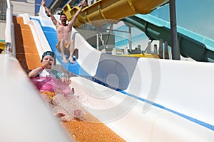 Dad and daughter are happy going down slide in water park.