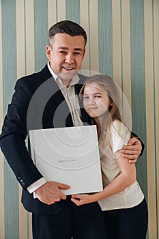 A dad and daughter hold a photo book in a white leather cover