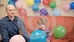 Dad and daughter inflate balloons, play with them. They are contented and happy