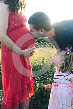 Dad and daughter are looking at a pregnant belly. The family is expecting a second child. The little sister is waiting for her