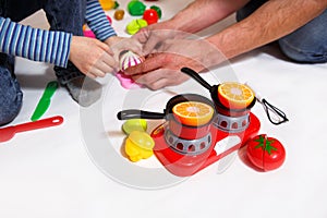 Dad and daughter play with sliced plastic vegetables and fruits with Velcro, cooks food on a toy stove in a bowl. Children`s