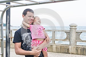 Dad and daughter playing promenade by the sea. young man, little girl hanging on the bar.