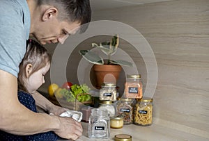 Dad and daughter pour cereal from a reusable bag into a glass jar. Storage in the kitchen