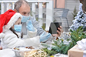 Dad and daughter in protective medical masks and a Santa hat wish Merry Christmas via messenger. Safe happy new year`s and Merry