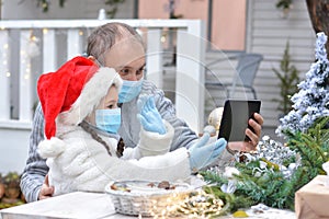 Dad and daughter in protective medical masks and a Santa hat wish Merry Christmas via messenger. Safe happy new year`s and Merry