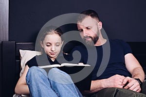 Dad and daughter are reading the Bible book together. Family. A happy child is smiling while sitting on the bed.