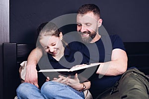 Dad and daughter are reading the Bible book together. Family. A happy child is smiling while sitting on the bed.