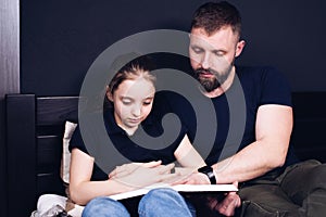 Dad and daughter are reading the Bible book together. Family. A happy child is smiling while sitting on the bed.