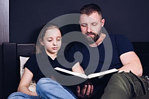 Dad and daughter are reading the Bible book together. Family. A happy child is smiling while sitting on the bed.