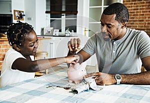 Dad and daughter saving money to piggy bank
