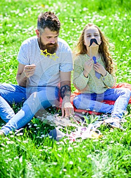 Dad and daughter sits on grass at grassplot, green background. Child and father posing with eyeglases and muastache