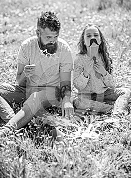 Dad and daughter sits on grass at grassplot, green background. Child and father posing with eyeglases and muastache