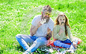 Dad and daughter sits on grass at grassplot, green background. Child and father posing with eyeglases and mustache photo photo