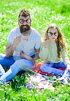 Dad and daughter sits on grass at grassplot, green background. Child and father posing with eyeglases photo booth